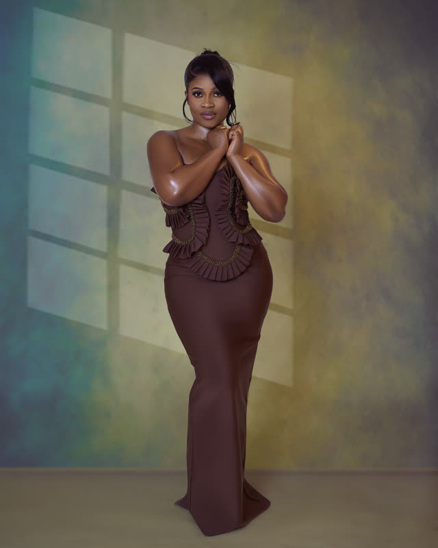 Full-length studio portrait of a woman in a fitted brown ruffled gown against a soft window-lit backdrop