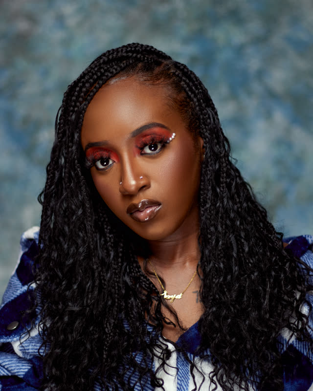 Close-up beauty portrait of a woman with long braids, red eyeshadow, and a blue plaid jacket