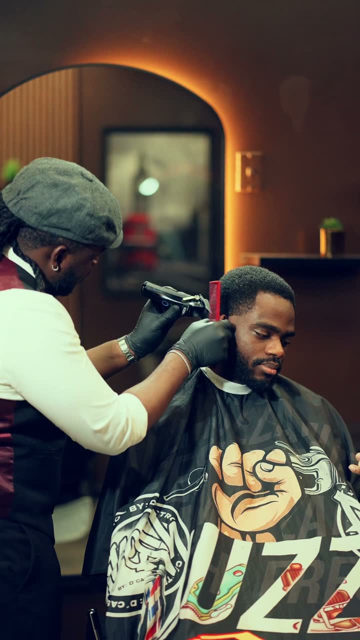 Film still: a barber shaping a client's hairline with clippers in a warm barbershop